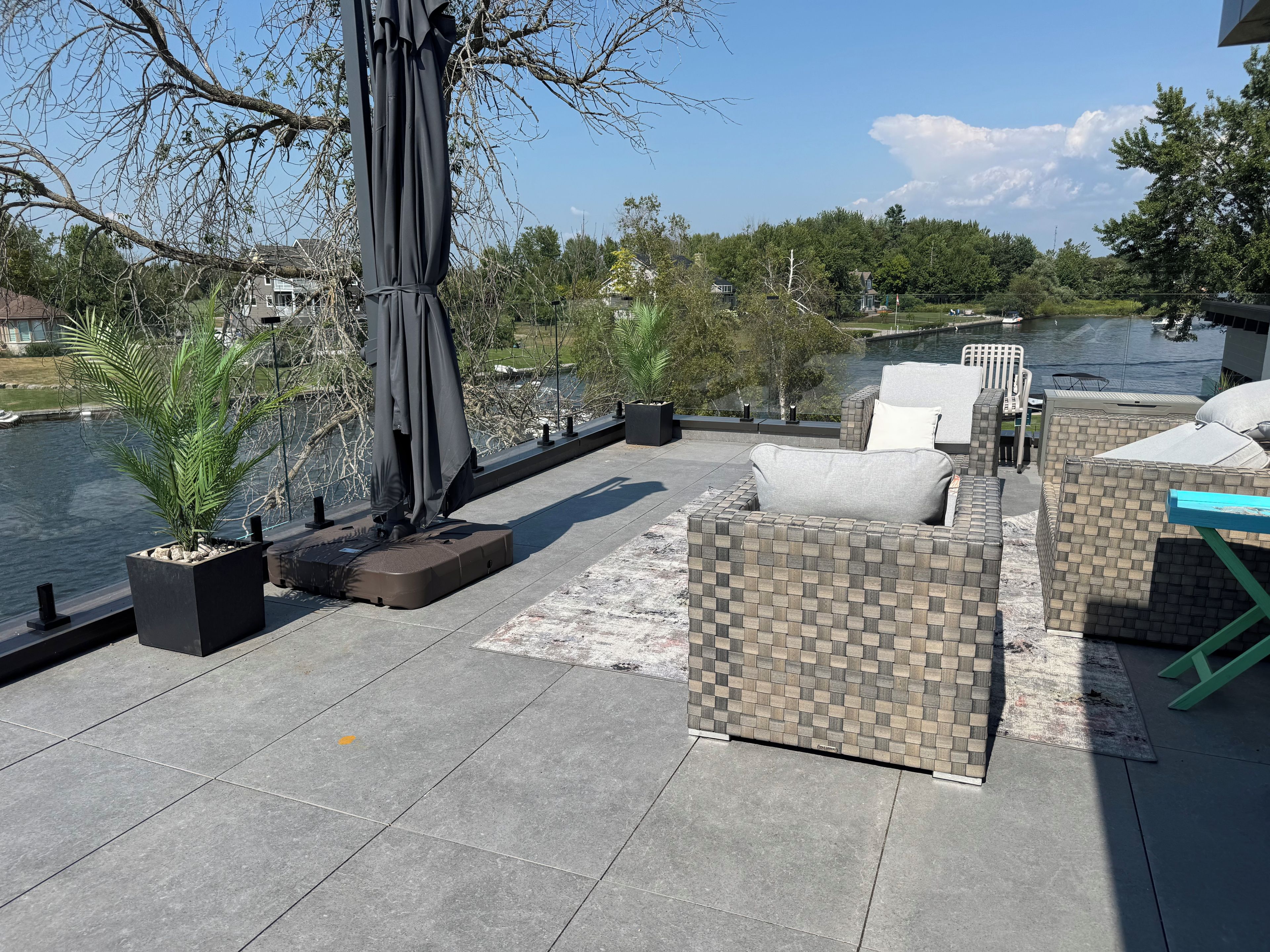 An outdoor seating area with a view of a body of water, a covered umbrella, and a potted plant.