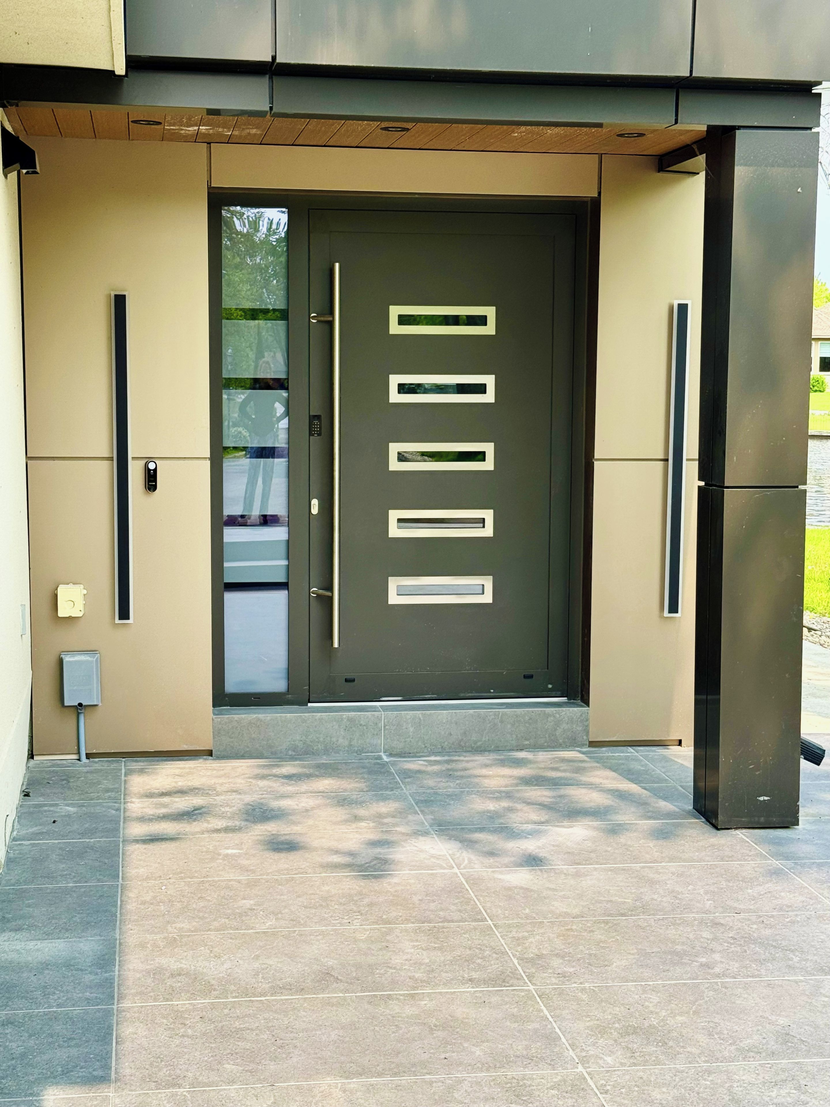 Entrada de un edificio moderno con una puerta de color oscuro, tiradores horizontales y un panel de vidrio.