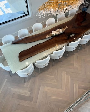 A modern dining area with a long wooden table, white chairs, and a chandelier. - Modern Waterfront Oasis. Sunsets • Serenity • Dock (Brechin)