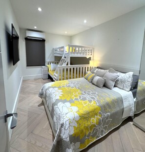 Un dormitorio con una cama litera, una cama con ropa de cama floral, una mesita de noche y un televisor montado en la pared.