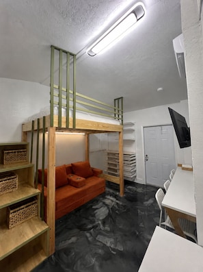 Ein Stockbett mit Schreibtisch und Regalen, ein Sofa und eine Tür in einem Zimmer mit Marmorboden.