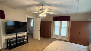 A bedroom with a bed, a TV on a stand, a ceiling fan, and a door leading to another room. - Peaceful Downtown Abode (Americus)
