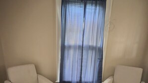 A room with beige walls, a large window with sheer curtains, and two beige armchairs with wooden legs. - Peaceful Downtown Abode (Americus)