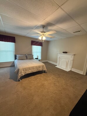 A bedroom with a bed, a ceiling fan, a fireplace, and a window with blinds.