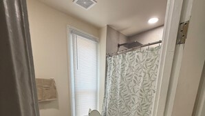 A bathroom with a toilet, a shower curtain, and a window with blinds. - Peaceful Downtown Abode (Americus)