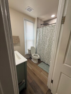 A bathroom with a toilet, a shower curtain, and a window with blinds.