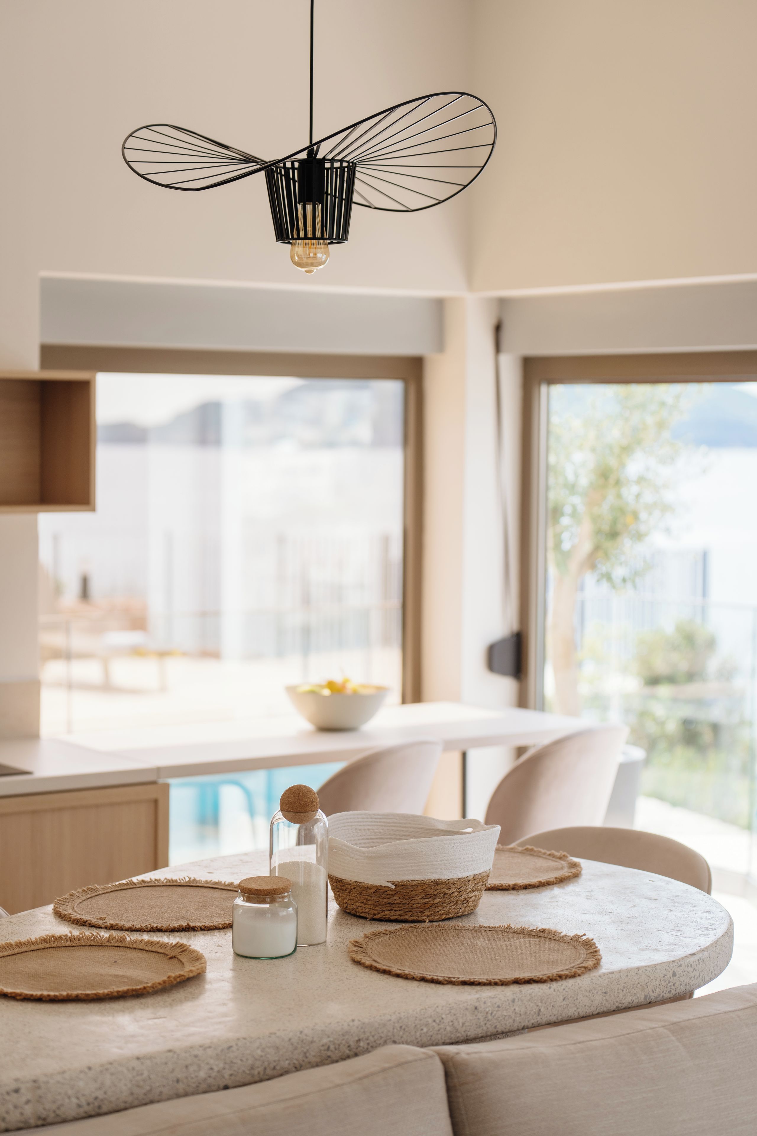 Una cocina moderna con una lámpara de techo negra original, una mesa de comedor con individuales tejidos y vistas al exterior.