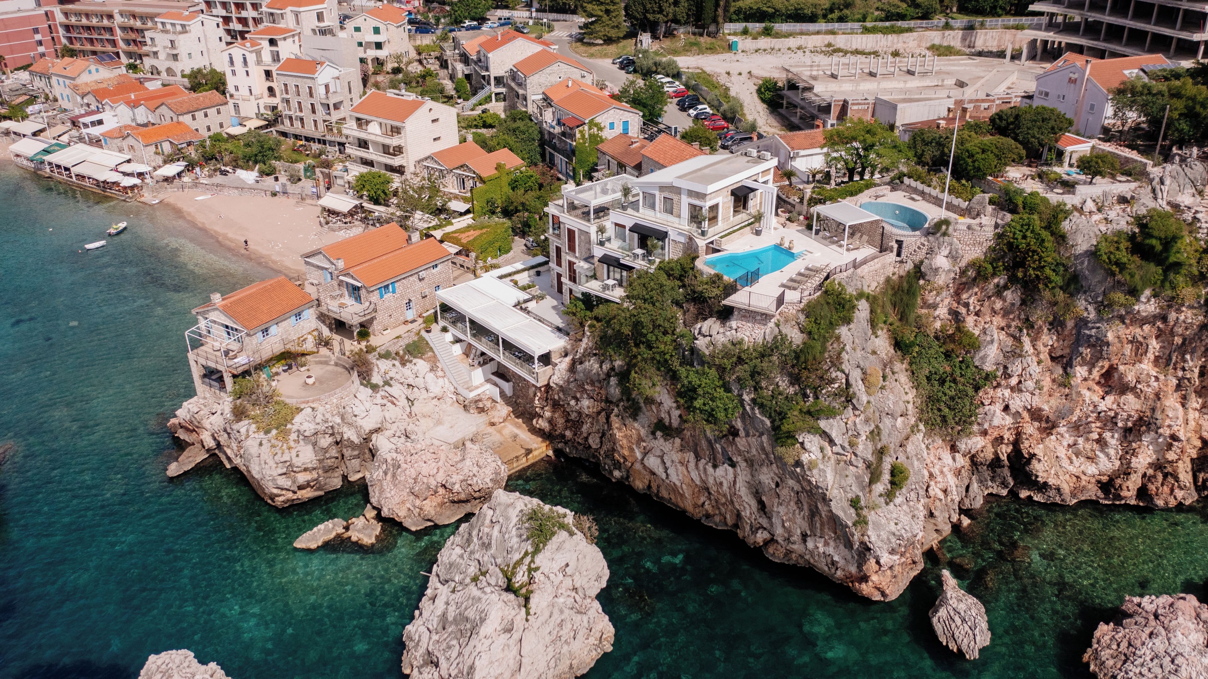 A coastal property with a swimming pool, multiple buildings, and a rocky cliff.