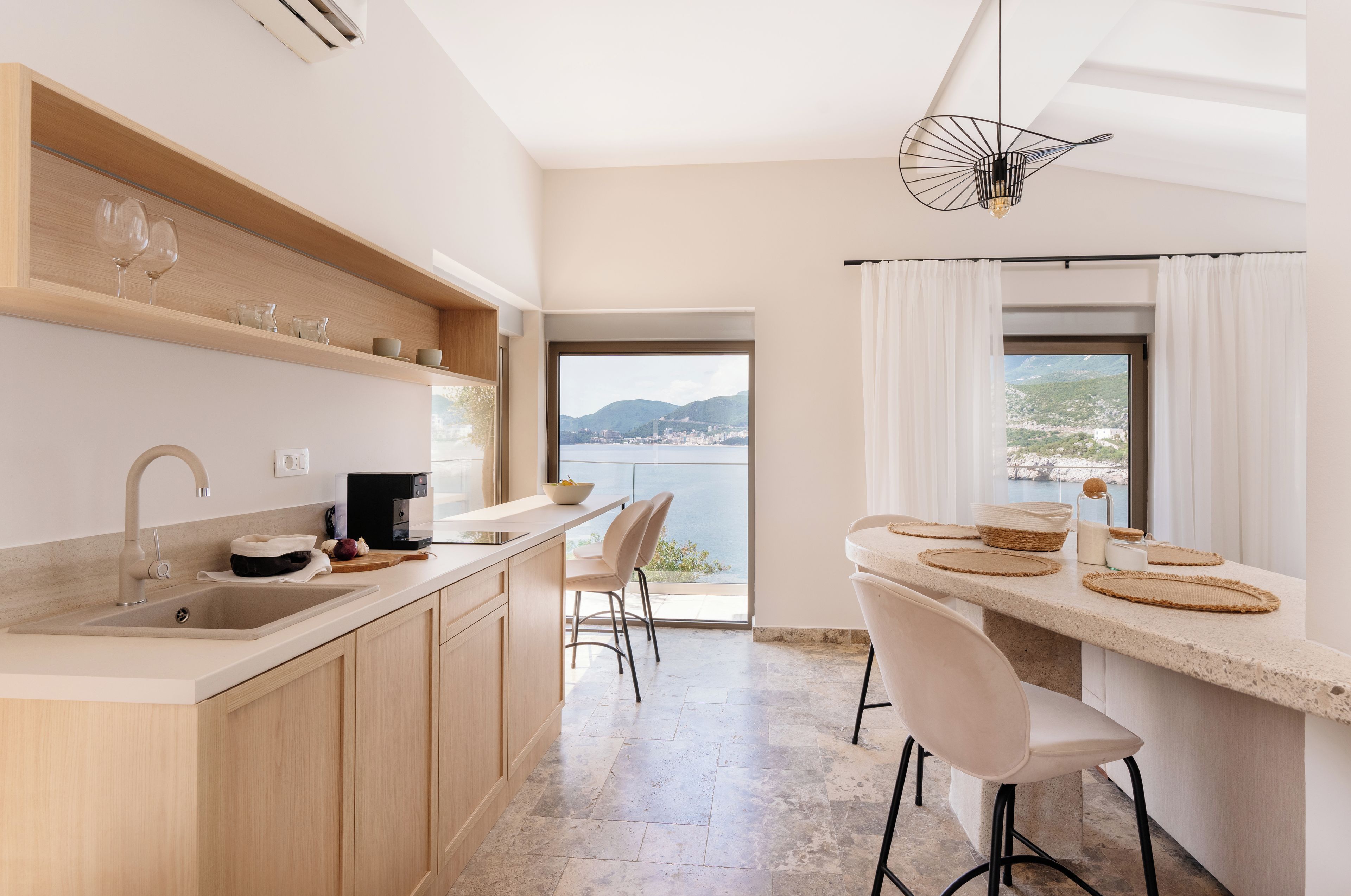 Una cocina moderna con vista al mar, un comedor con taburetes de bar y una lámpara colgante.
