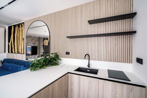 A modern kitchen with a built-in sink, wooden panel wall, and a blue sofa in the adjacent living area.