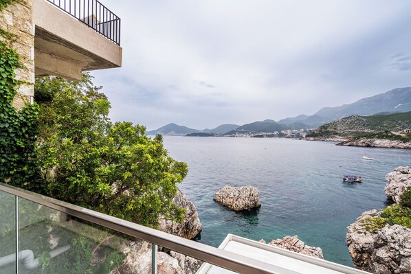 A coastal view with a balcony overlooking the sea, rocky formations, and distant mountains.