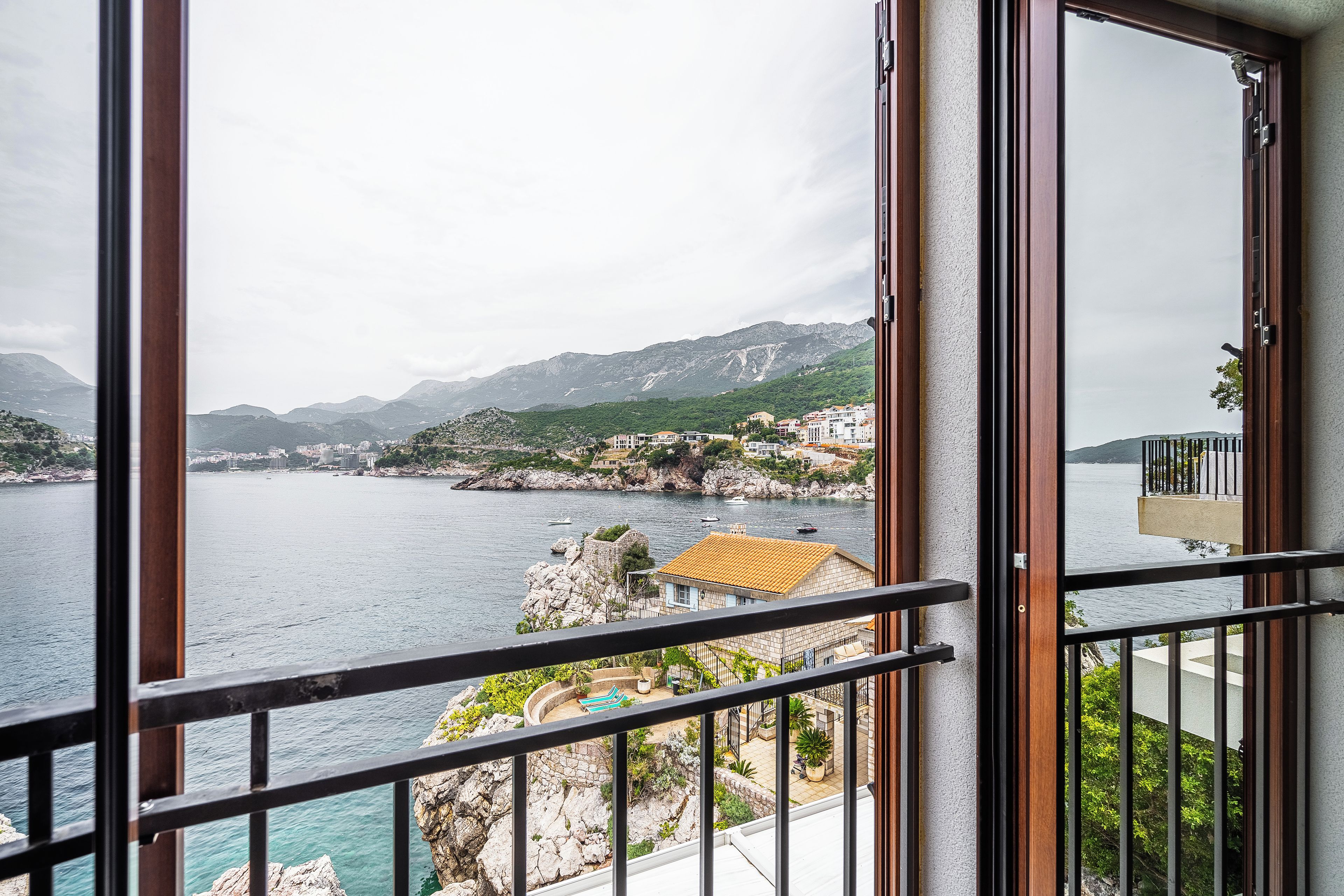 A balcony with a view of a coastal town, rocky terrain, and a body of water.