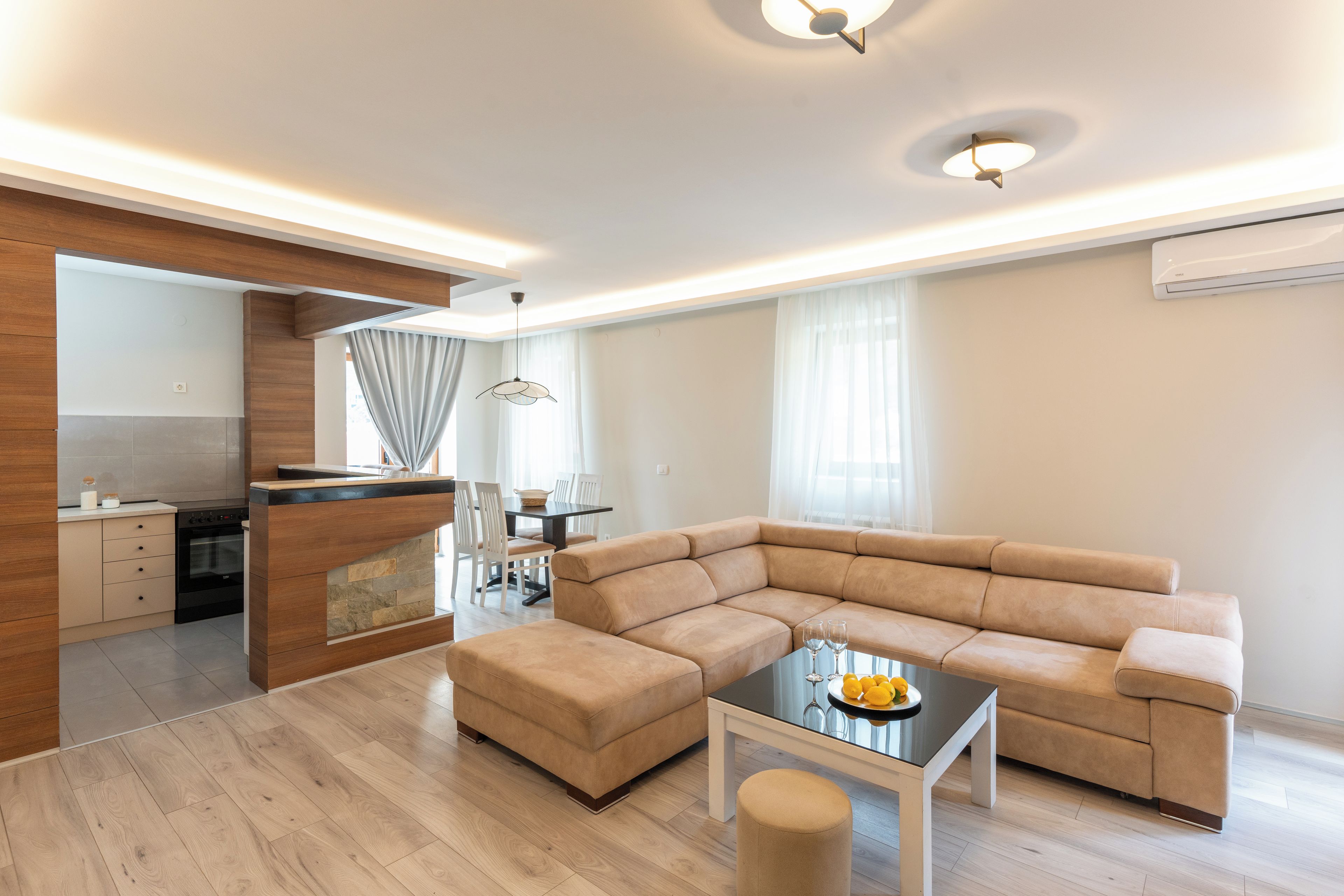 A modern living room with a sectional sofa, a glass coffee table, and a kitchen area with a dining set.