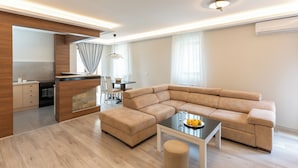 Una sala moderna con un sofá modular, una mesa de centro de vidrio y una zona de cocina con comedor.