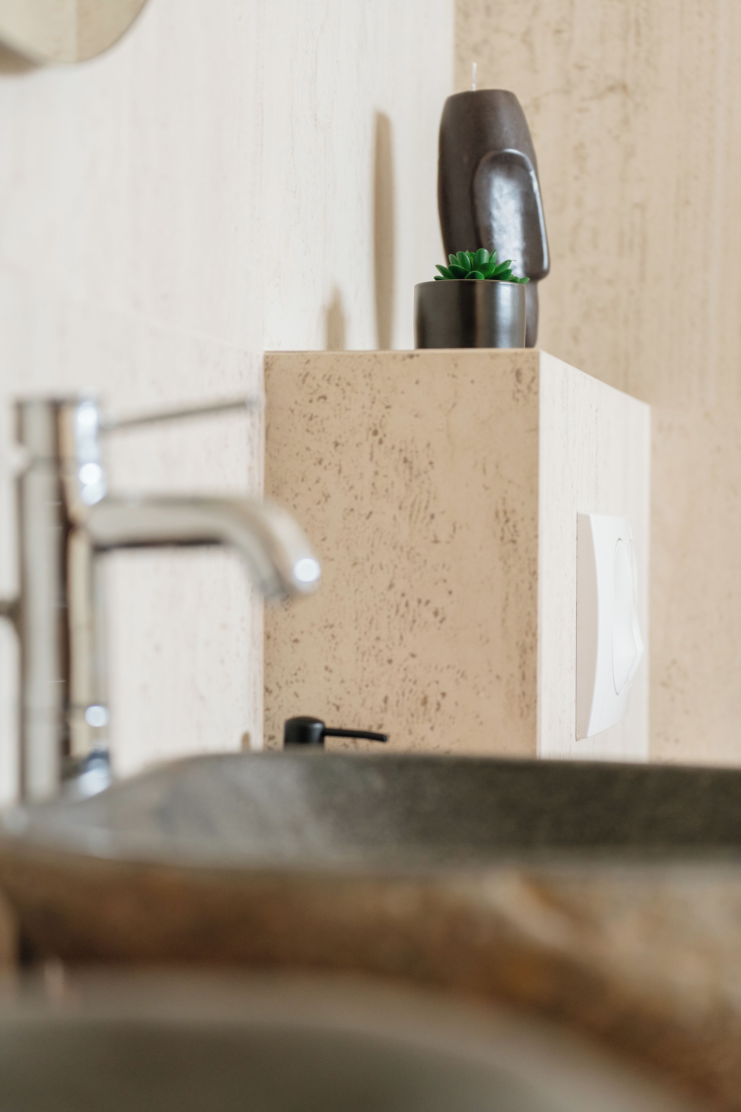 Un lavabo de salle de bain avec un robinet moderne, une petite plante en pot et un distributeur de savon.