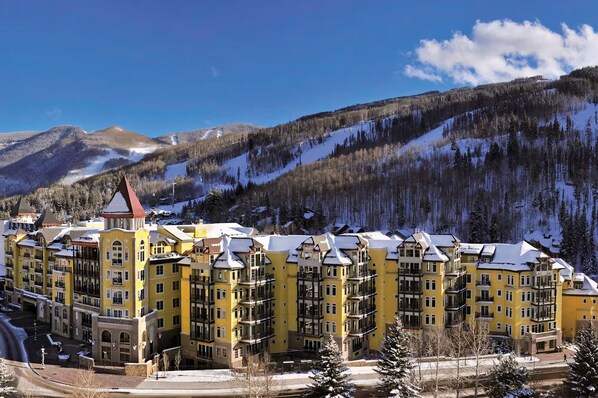 Un hotel de varios pisos con fachada amarilla, situado en una zona montañosa con laderas nevadas.