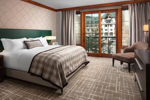 A hotel room with a large bed, a chair, a desk, and a view of a building through a glass door. - The Ritz-Carlton Club Vail 3 Bedroom Residence (Vail)
