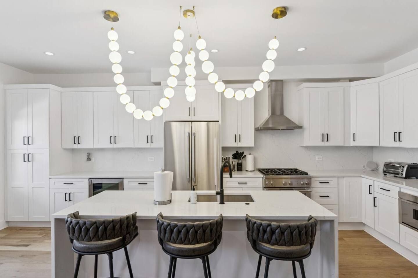 A modern kitchen with white cabinets, a central island, and a unique pendant light fixture.