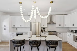 A modern kitchen with white cabinets, a central island, and a unique pendant light fixture. - Lux Chicago House with 6 Bedrooms / Garage / Yard / Game Room (Chicago)