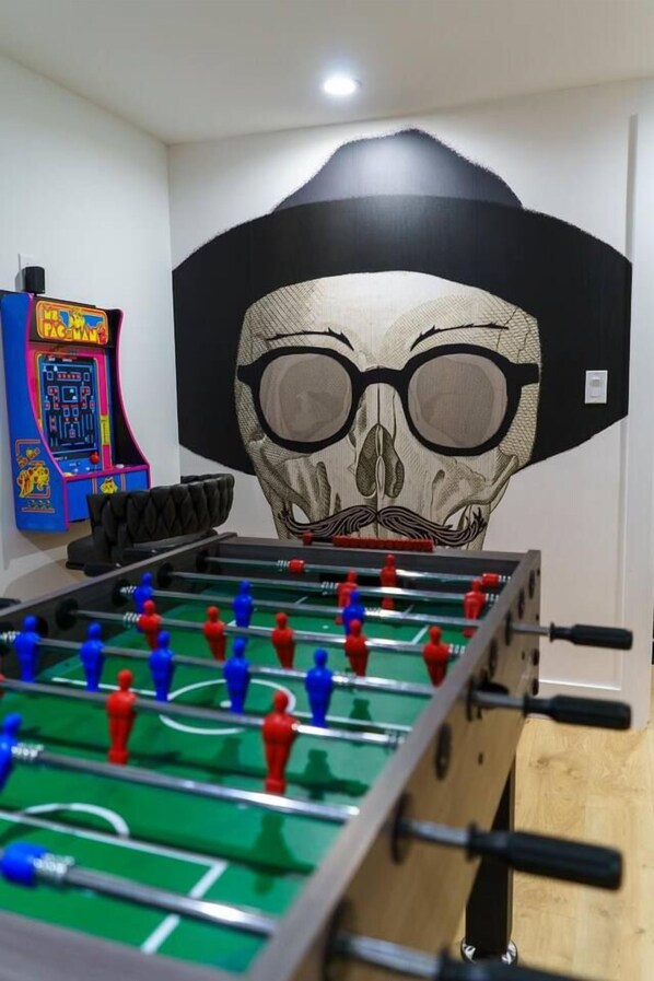 A room with a foosball table, a Pac-Man arcade machine, and a large skull mural on the wall.