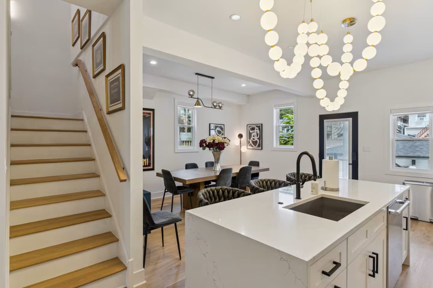 A modern kitchen with a central island, wooden staircase, and dining area with chairs and a table.