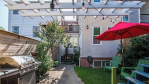 A backyard with a barbecue grill, patio furniture, and a pergola with string lights. - Sojourn 1 Block to Metro, Cap Hill Garden Flat (Washington)