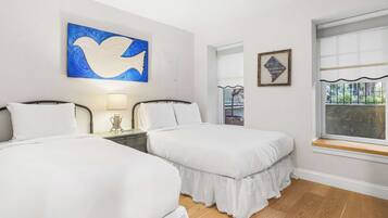 A hotel room with two beds, a large window, and artwork on the walls.