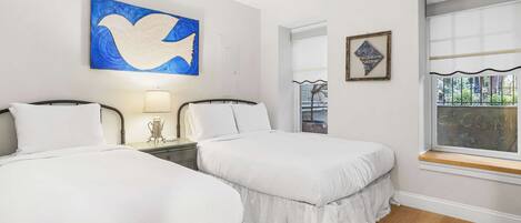 A hotel room with two beds, a large window, and artwork on the walls.