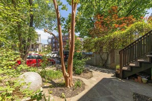 A courtyard with a stone pathway, trees, and a staircase leading to an upper level.