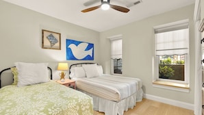 A bedroom with two beds, a ceiling fan, artwork, and a window with a view. - Sojourn 1 Block to Metro, Cap Hill Garden Flat (Washington)