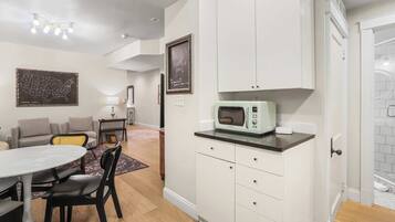 A compact kitchen with white cabinets, a vintage microwave, and a dining area with a round table and chairs.