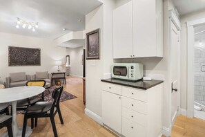 A compact kitchen with white cabinets, a vintage microwave, and a dining area with a round table and chairs.