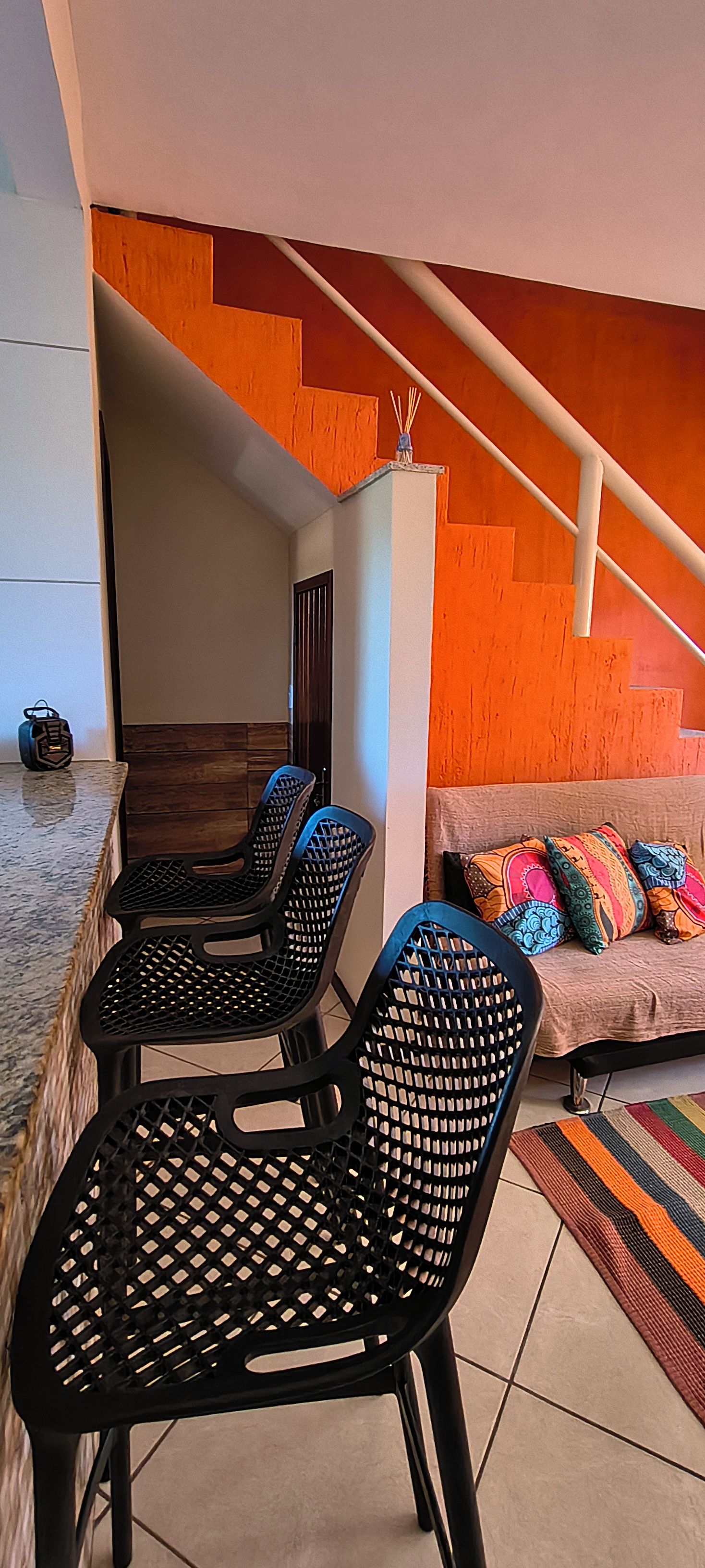 Uma sala de jantar com cadeiras pretas, uma mesa de madeira e um sofá com almofadas coloridas.