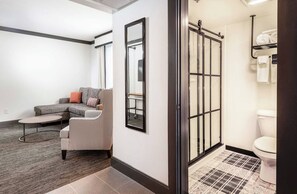 Ein modernes Hotelzimmer mit grauem Sofa, einem Hounds-Tooth-Sessel, einem kleinen runden Tisch und einem großen Spiegel.