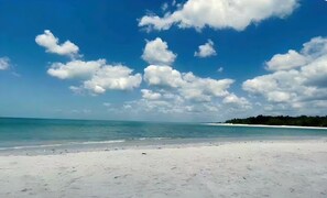 Ein Strand mit blauem Himmel und vereinzelten Wolken.