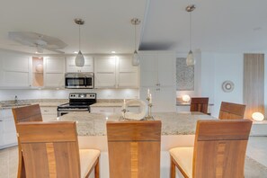 A modern kitchen with white cabinetry, a central island with chairs, and pendant lighting. - Redesigned Vanderbilt Beach Residence - Gulf & Sunset Views - Walk to Beach (Naples)