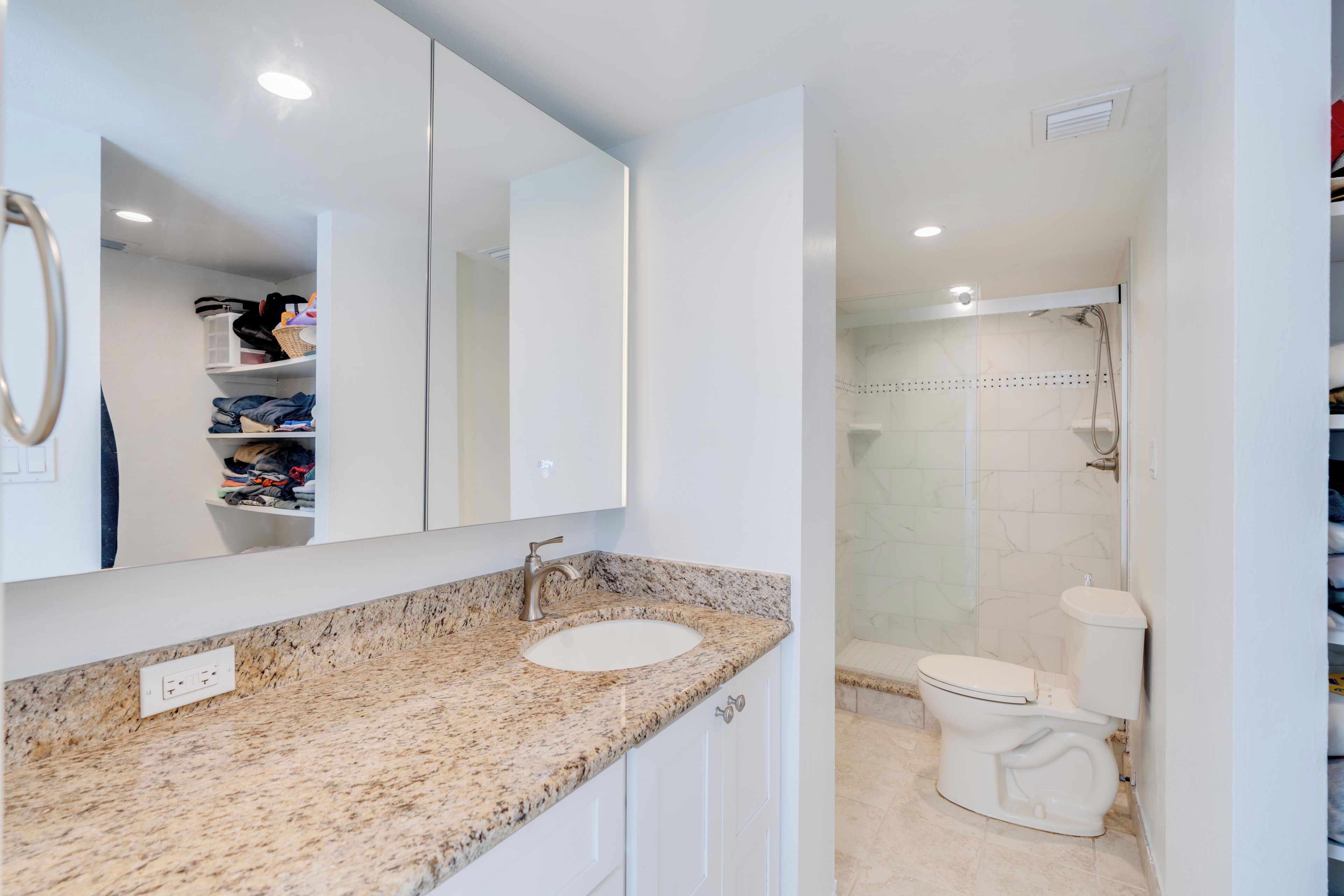 A bathroom with a granite countertop, a white sink, a mirror, a toilet, and a shower area.