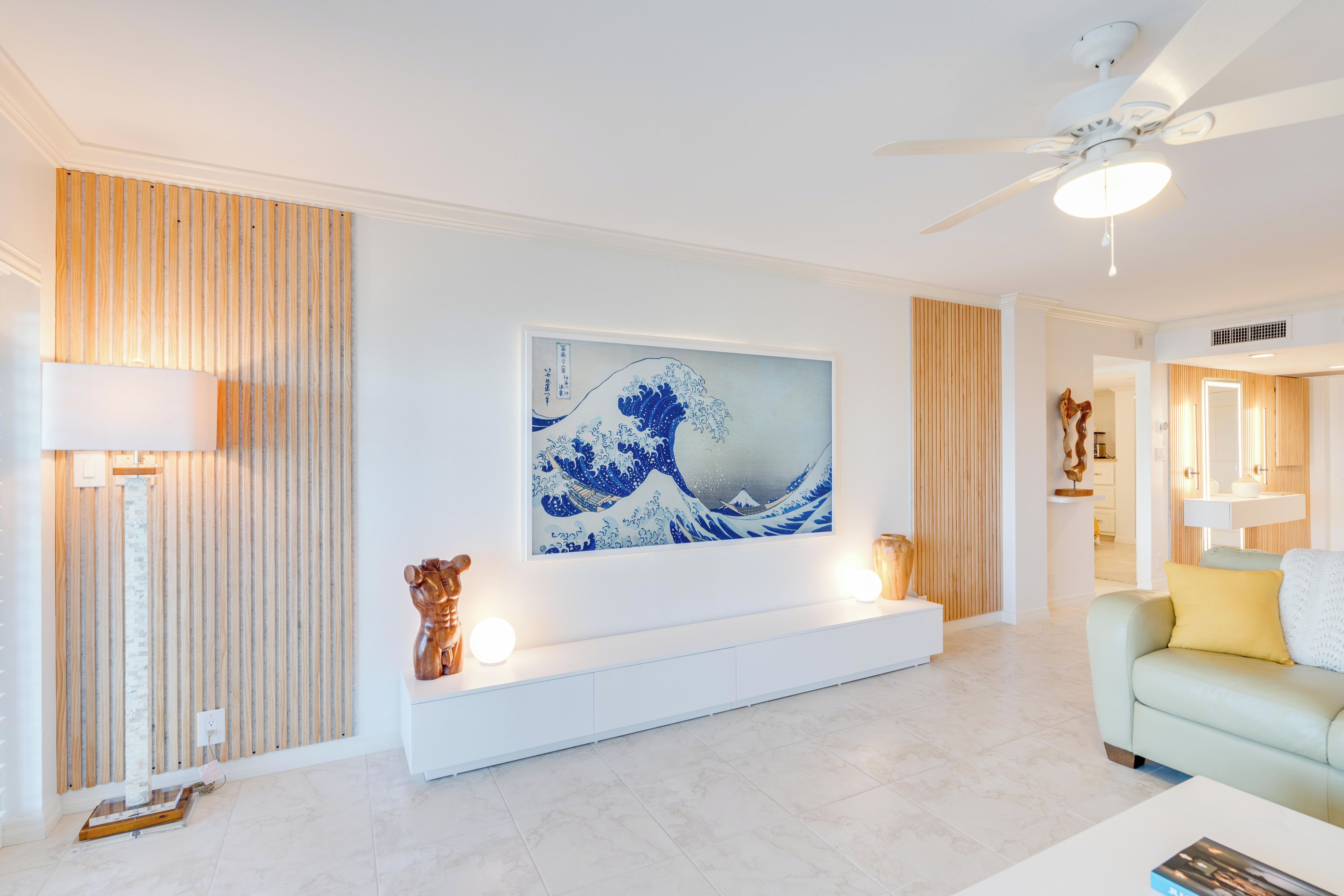 A modern living room with a large wave painting, a ceiling fan, and a minimalist design.