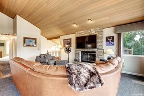 A living room with a stone fireplace, leather sofa, and a television mounted above it. - Tahoe Keys Waterfront Retreat | Private Hot Tub, Boat Dock & Mountain Views (South Lake Tahoe)