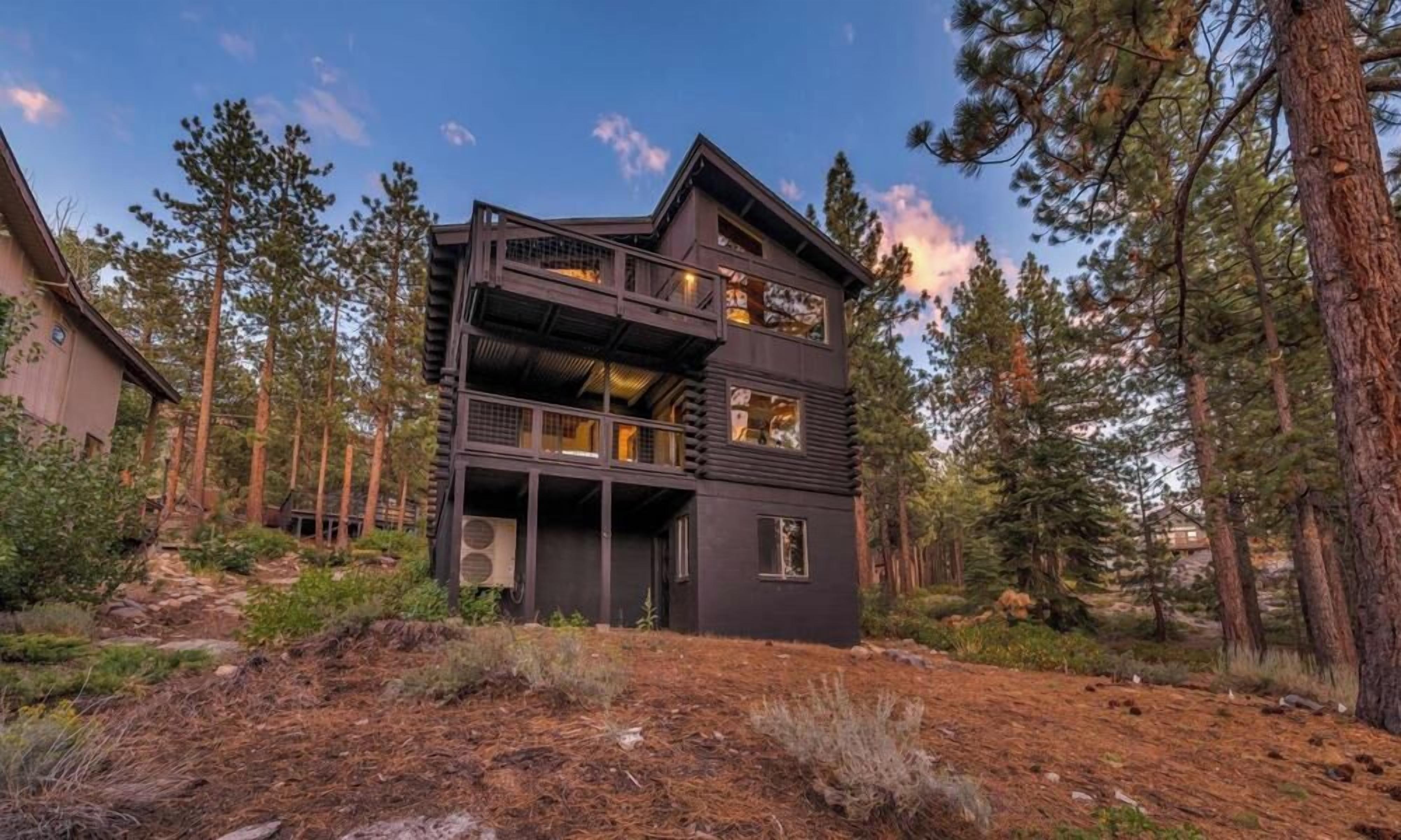 Cabana de vários níveis com exterior escuro, rodeada por uma área arborizada.