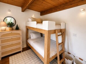 Un lit superposé avec une structure en bois, une table de chevet avec une lampe et une petite plante.