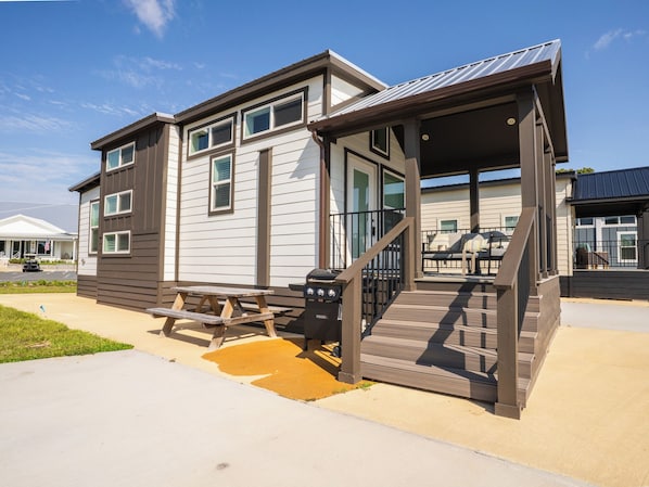 A two-story building with a covered porch and a barbecue grill.