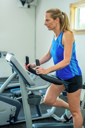 A person using a stationary bike in a gym with exercise equipment and a window in the background. - The Tannehill - Citrus Loft Cabin - Grill - Pool - Hot Tub - Bar - Lake - Gym (Crystal River)