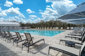 A swimming pool with lounge chairs and umbrellas, surrounded by trees and a clear sky. - The Tannehill - Citrus Loft Cabin - Grill - Pool - Hot Tub - Bar - Lake - Gym (Crystal River)