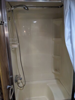 A shower area with a handheld showerhead, a wall-mounted faucet, and a shower curtain. - Charming 2-bedroom recreational vehicle in enjoyable Sequim location (Sequim)