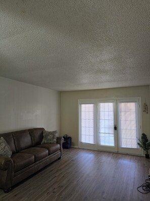 A living room with a brown leather sofa, a white door with blinds, and a wooden floor. - Adorable 1-bedroom condo with AC in beautiful Runaway Bay with lake views (Runaway Bay)