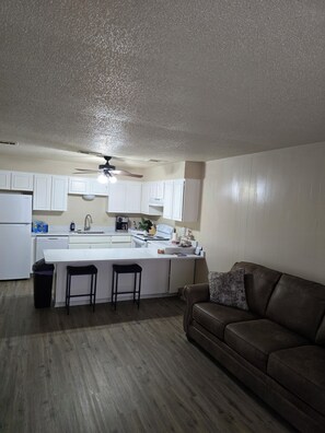 A compact kitchen with white cabinets, a central island, a ceiling fan, and a brown leather sofa. - Adorable 1-bedroom condo with AC in beautiful Runaway Bay with lake views (Runaway Bay)