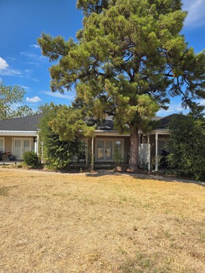 A residential house with a large pine tree in the front yard, a garage, and a well-maintained lawn. - Adorable 1-bedroom condo with AC in beautiful Runaway Bay with lake views (Runaway Bay)