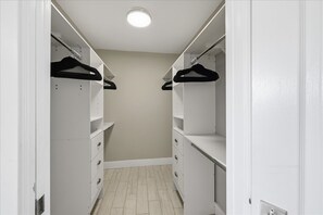 Un dressing avec des étagères blanches, des cintres noirs et un sol carrelé.