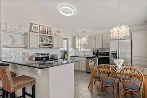 A modern kitchen with a central island, stainless steel appliances, and a dining area with wicker chairs. - Beautiful Beach home in a gated neighborhood located near everything! (Panama City Beach)